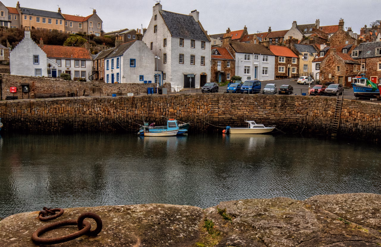 Fishing boats moored below traditional stone houses at Crail Harbour.