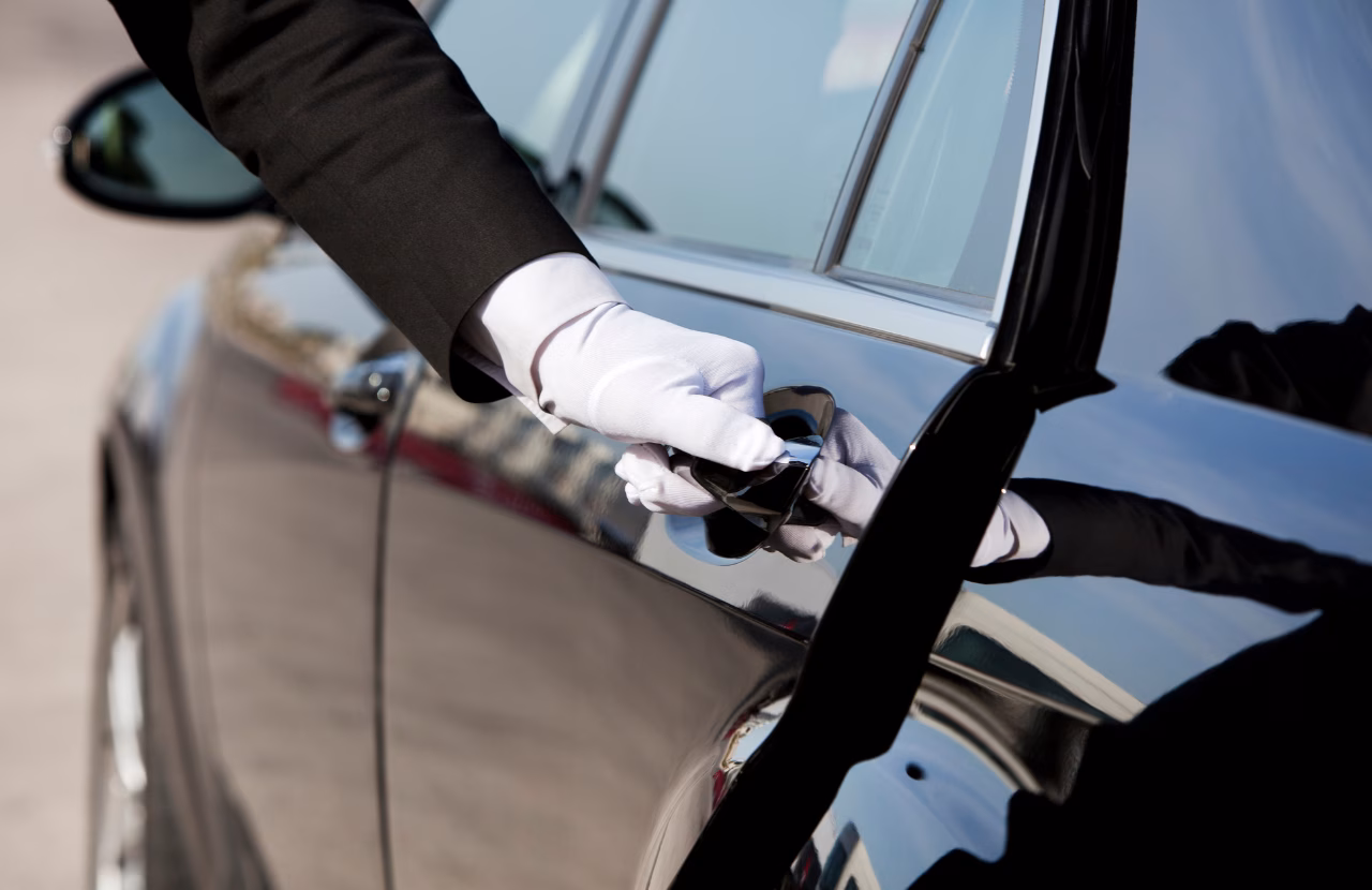 Chauffeur wearing white gloves opening a black car door.