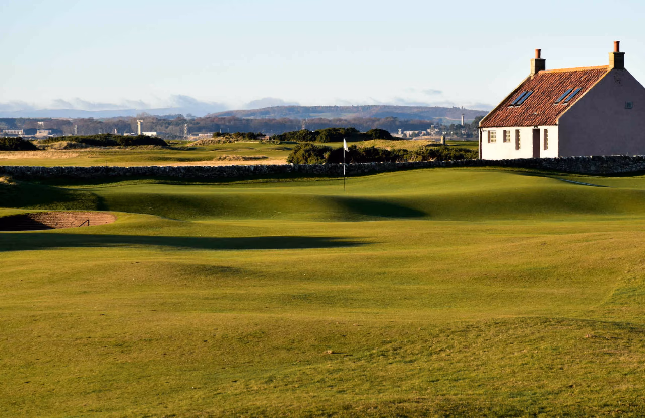 The Eden Course with a green, stone wall, and traditional white cottage.