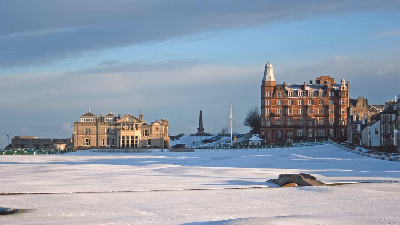 Snow-covered Old Course with the Swilcan Bridge and St Andrews buildings beyond.