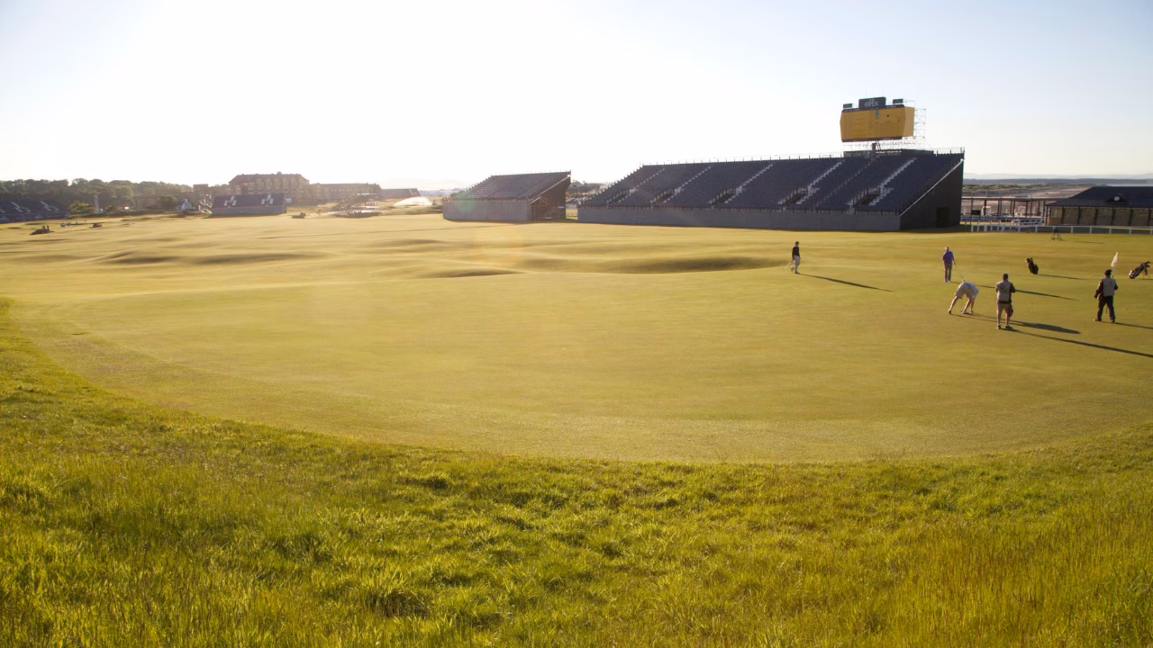 Golfers on the Old Course at St Andrews with Open Championship grandstands beside the fairway.